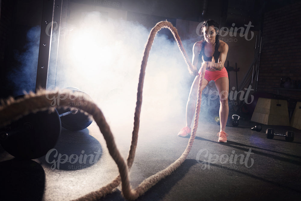 Determinated woman tossing ropes at gym