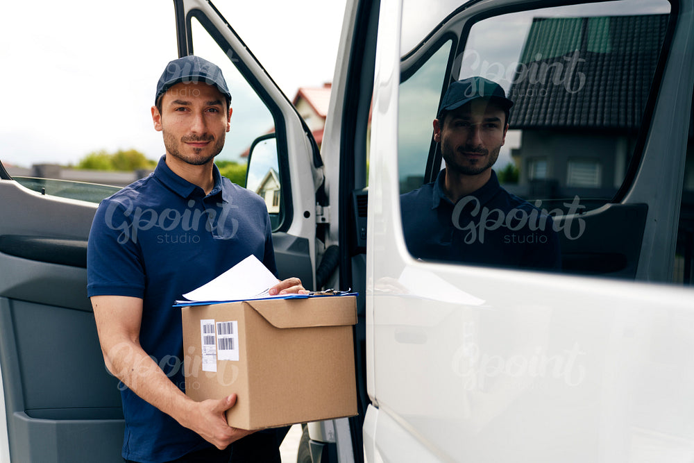 Portrait of courier holding cardboard box and documents