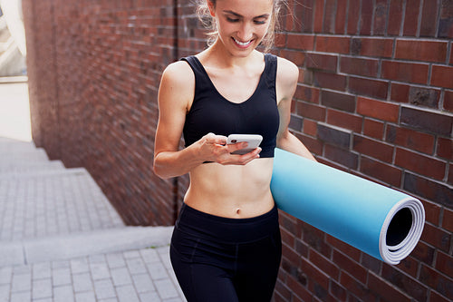 Smiling woman with mobile phone and exercise mat