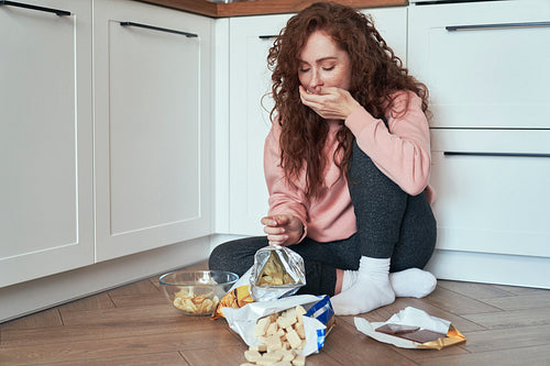 Young caucasian woman having eating disorder and eating greedily on the floor