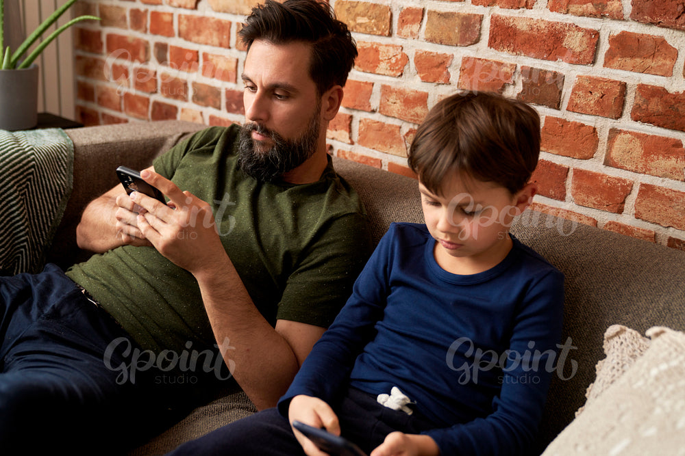 Father and son sitting with mobile phone at home