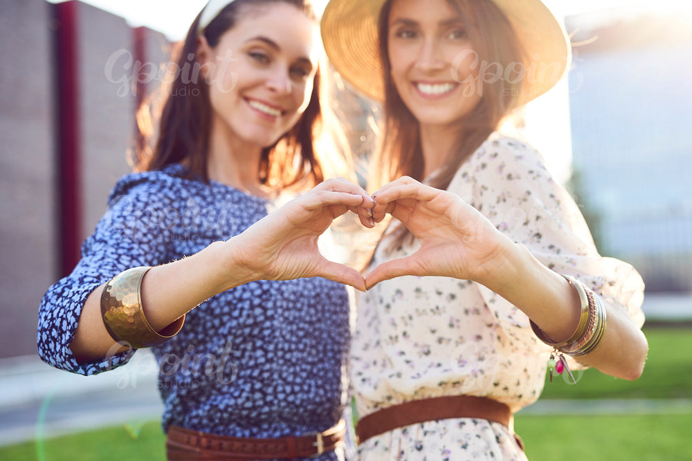 Two smiling woman making a heart out of a hand