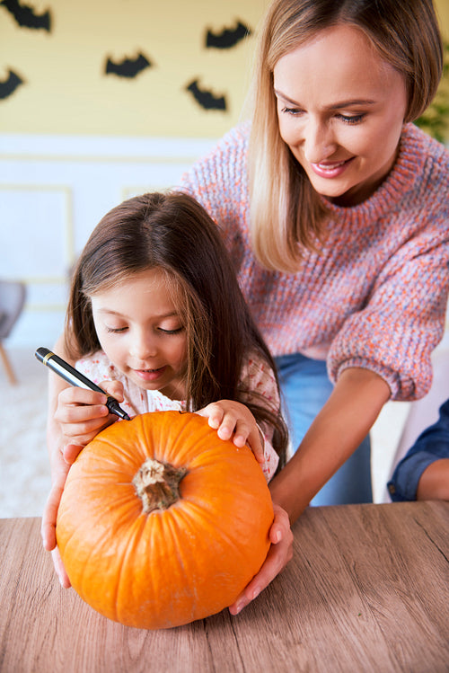 Cute girl drawing on pumpkin with mother