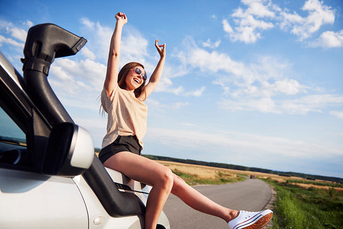 Woman with hands raised sitting on car