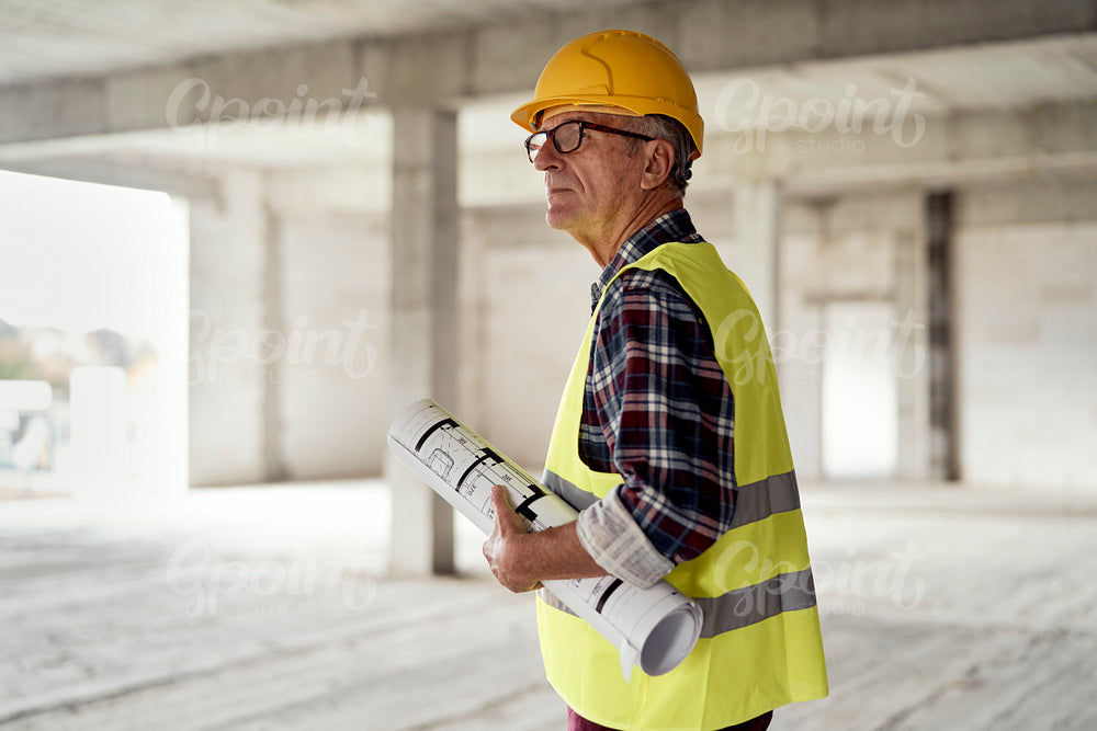 Caucasian senior engineer walking and holding plans on construction site