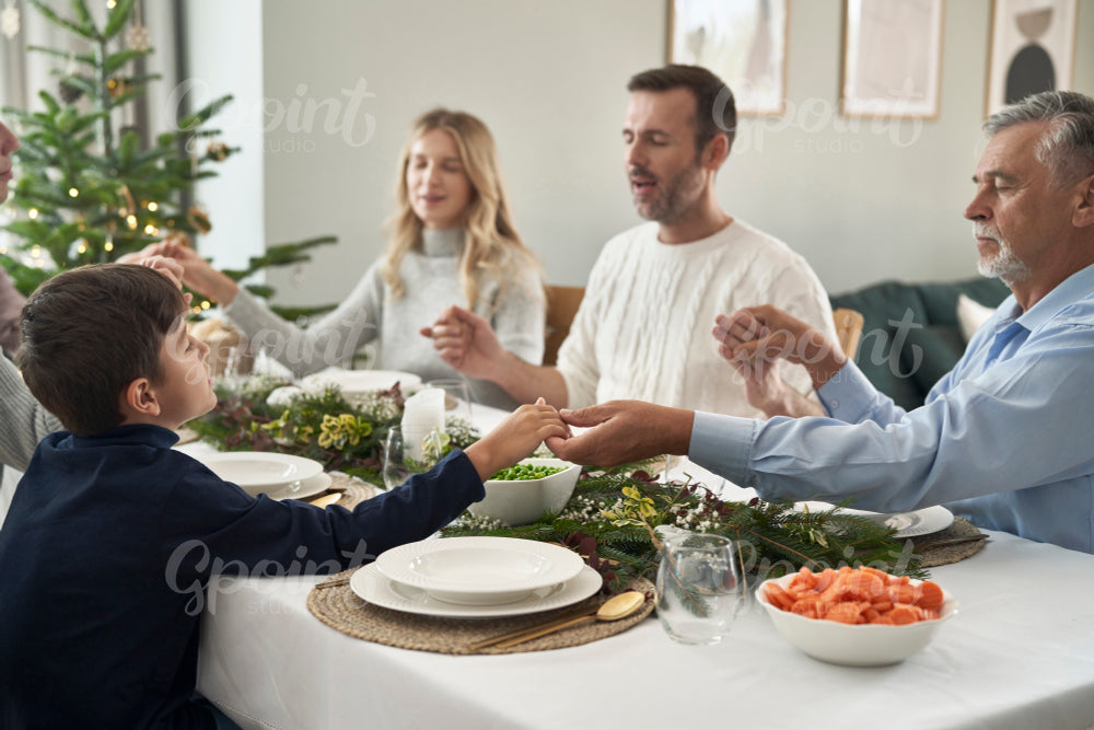 Caucasian multi generation family sitting around the table, holding hands and praying 