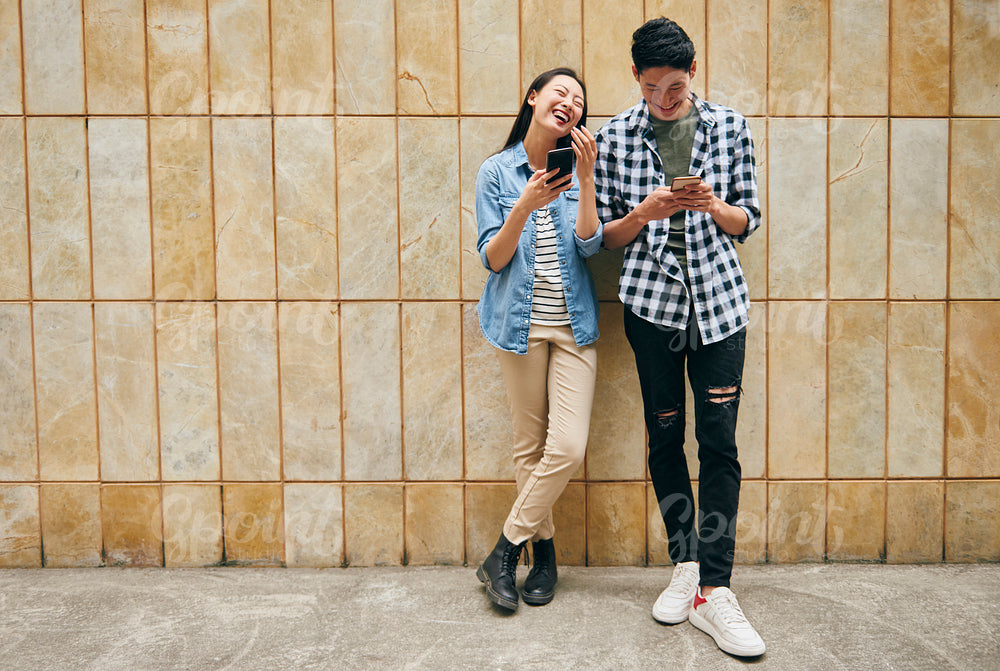 Young couple with mobile phone standing against the wall