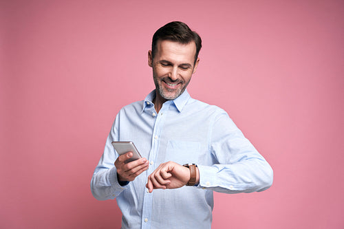 Studio shot of middle aged caucasian man using phone and checking time on watch
