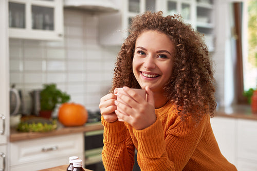 Smiling young woman drinking hot tea in the kitchen