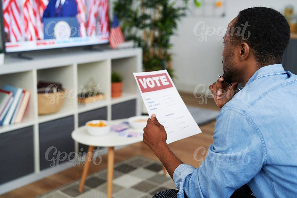 Black man watching tv and holding vote document