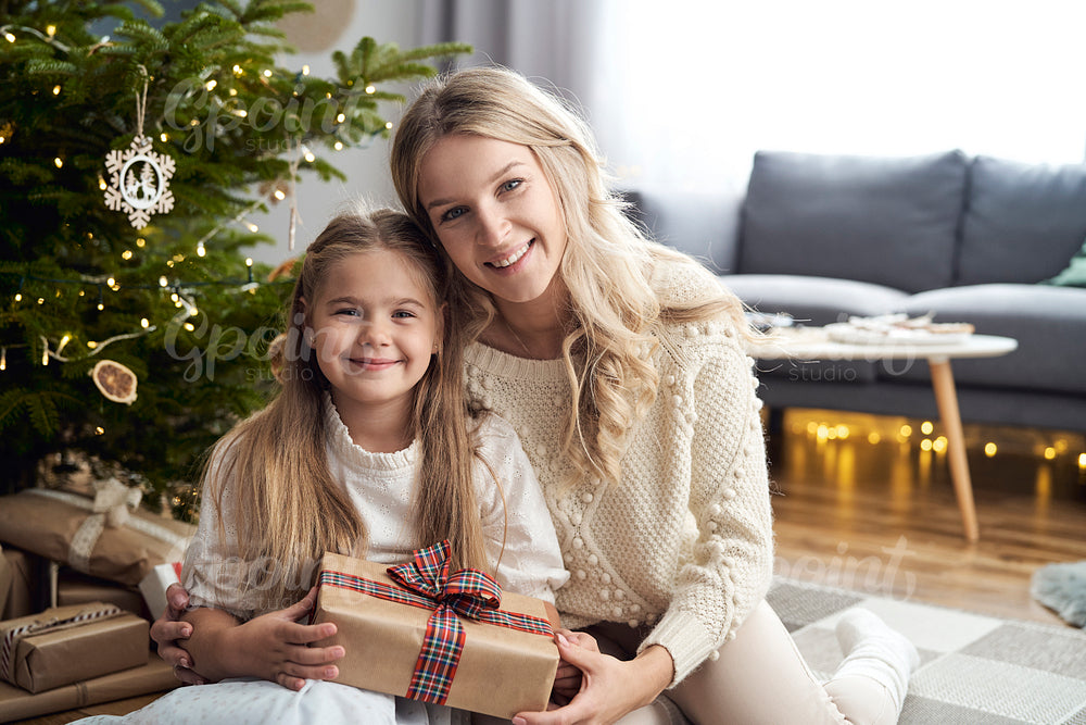 Portrait of caucasian girl and mother embracing each other and holding Christmas gift