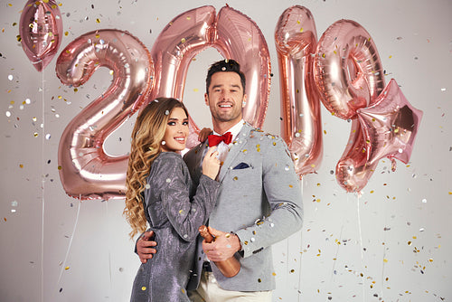 Portrait of couple with balloons and champagne under shower of confetti