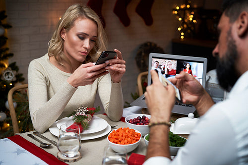 Couple spending Christmas time using mobile phone at the table