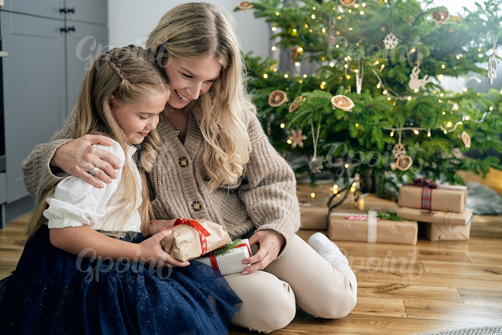 Caucasian girl and mother embracing each other and holding Christmas gift