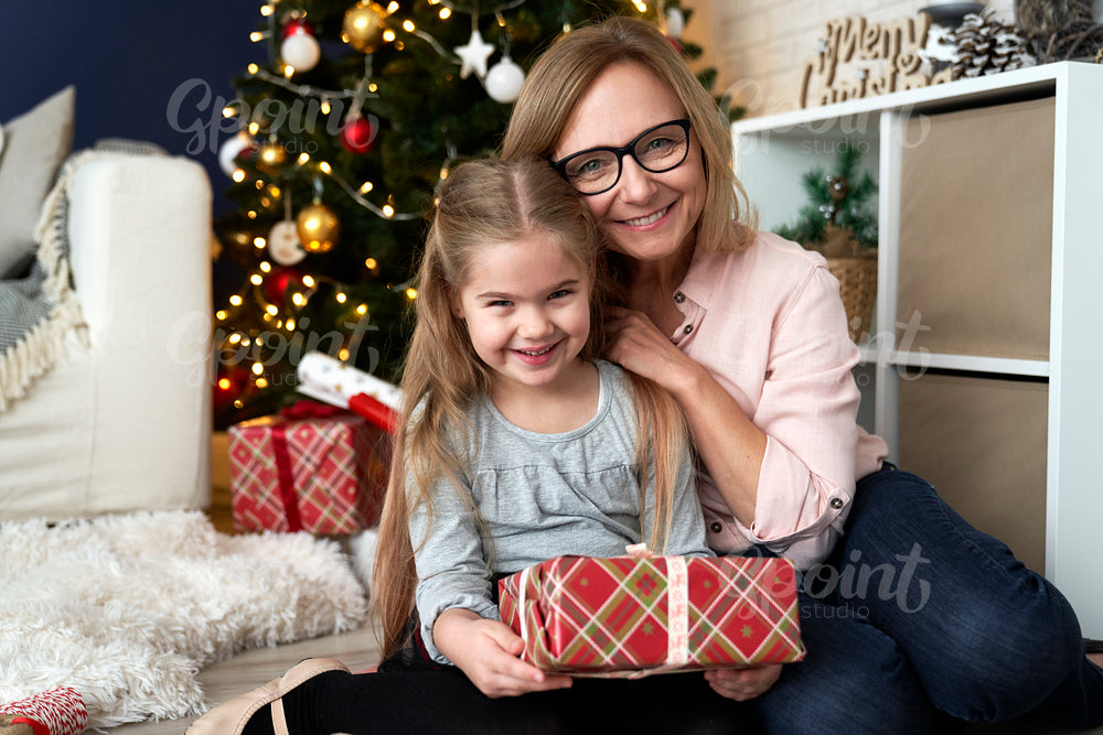 Portrait of grandma and granddaughter embracing beside a Christmas tree