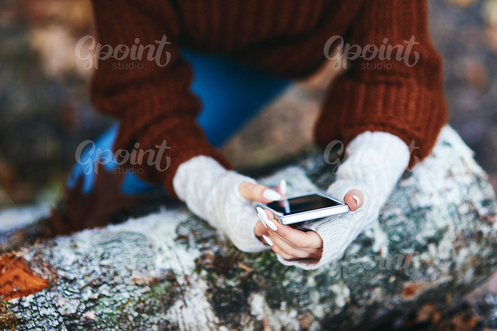 Woman’s hands using mobile phone in autumn forest