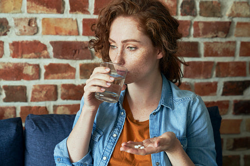 Caucasian red head woman about to take pills and drink water