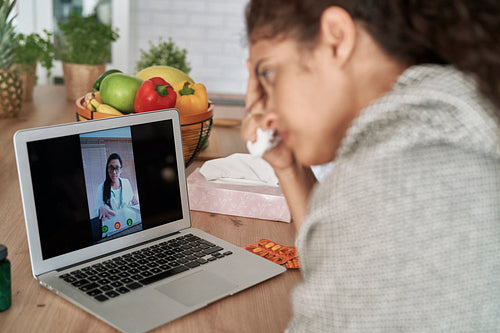 Sick woman talking video to doctor on laptop
