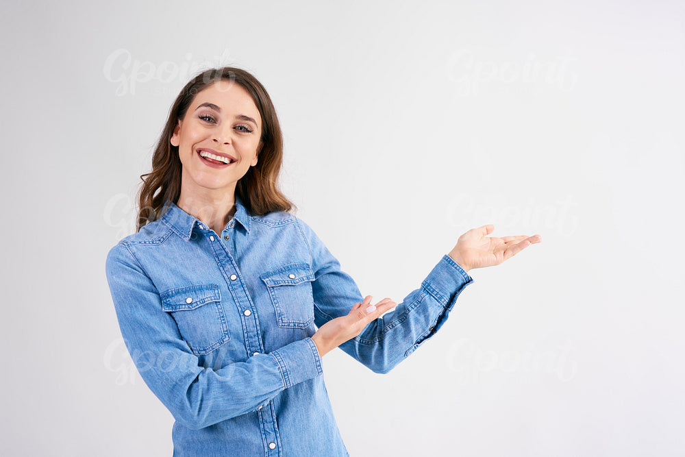 Smiling, young woman pointing at copy space at studio shot