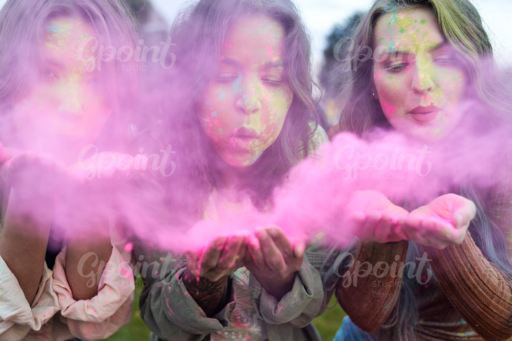 Group of women blowing coloured powder at music festival 