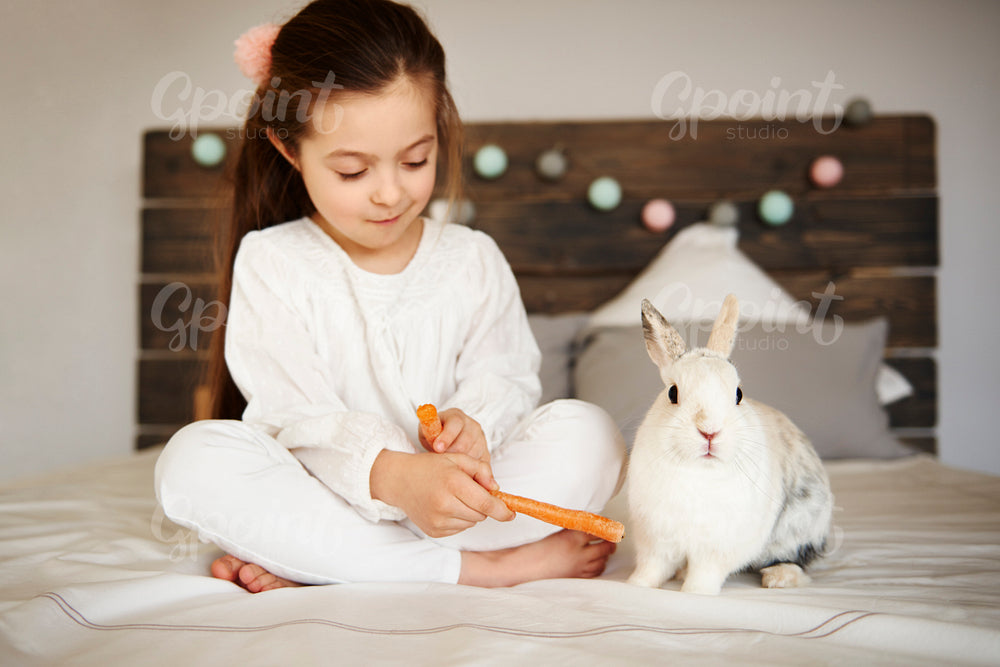 Girl feeding her rabbit on the bed
