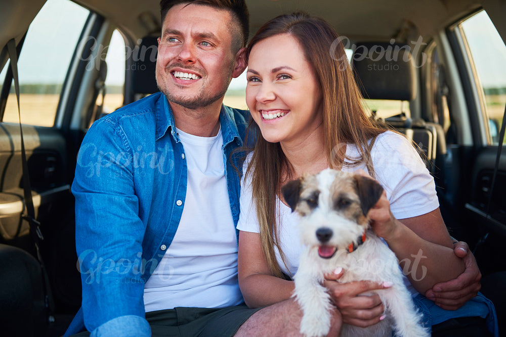 Smiling couple and their dog sitting in the car trunk