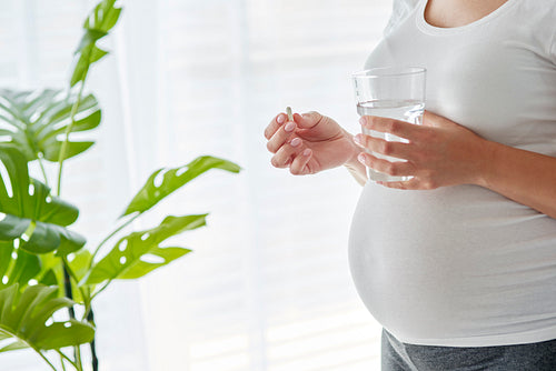 Pregnant woman about to take a pill and drink water