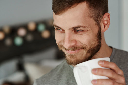 Smiling man drinking coffee at bedroom