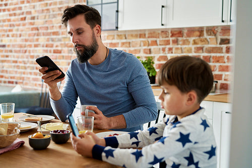 Focused father and son with mobile phone while breakfast