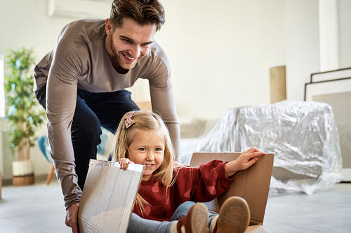 Caucasian father pushing little girl in paper box while moving house