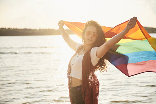 Beautiful young woman with rainbow flag at the beach
