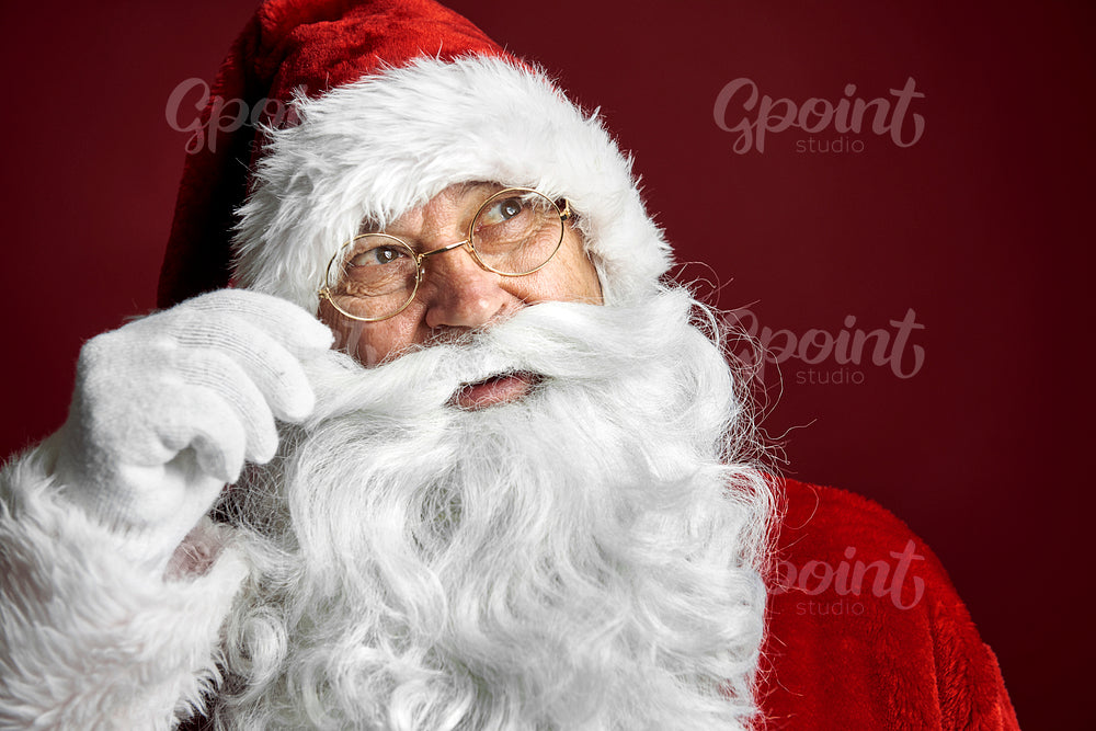 Smiling caucasian Santa Claus touching mustache on red background