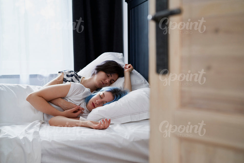 Lesbian couple sleeping together with the bedroom door open