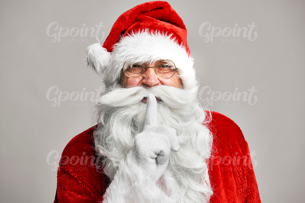 Santa Claus standing on the grey background and showing quiet sign 