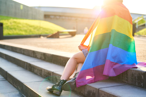 Unrecognizable woman with rainbow flag sitting on the stairs