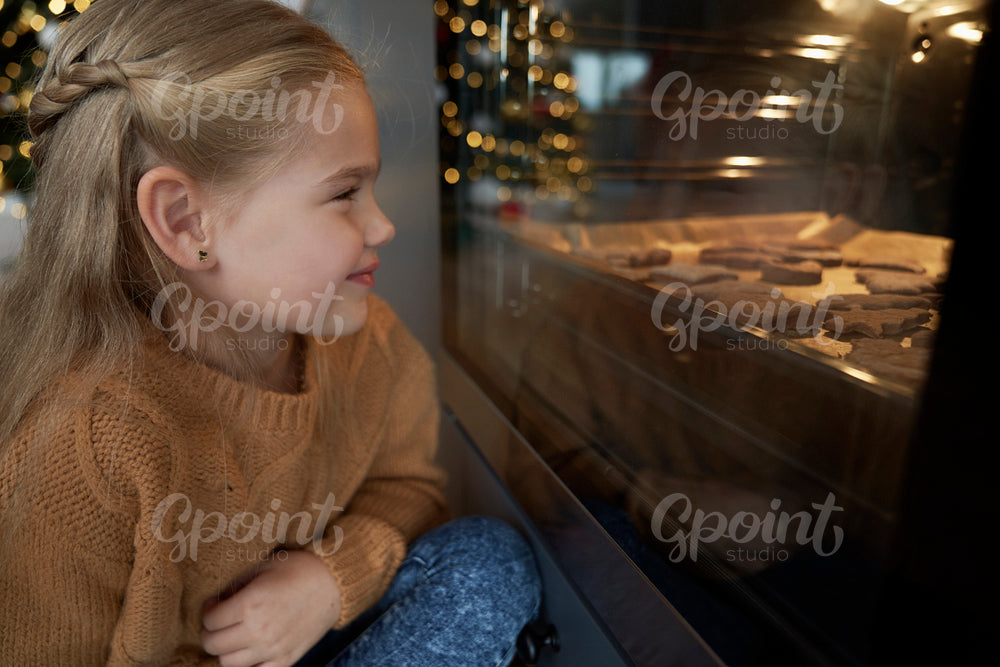 Little girl waiting next to oven for homemade cookies