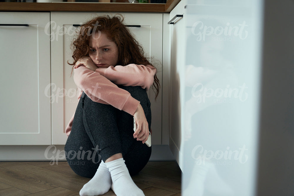 Thoughtful young caucasian woman sitting on floor in the kitchen
