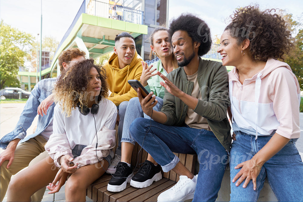 Group of young friends sitting and talking together with mobile phone