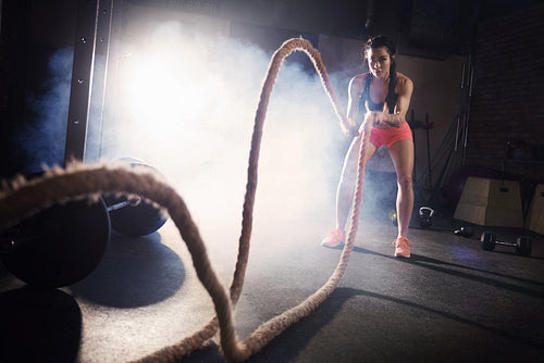 Determinated woman tossing ropes at gym