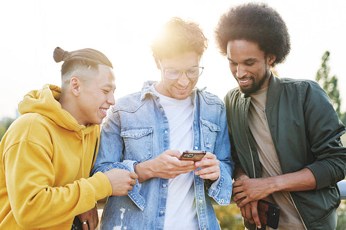 Three young smiling men standing and scrolling mobile phone