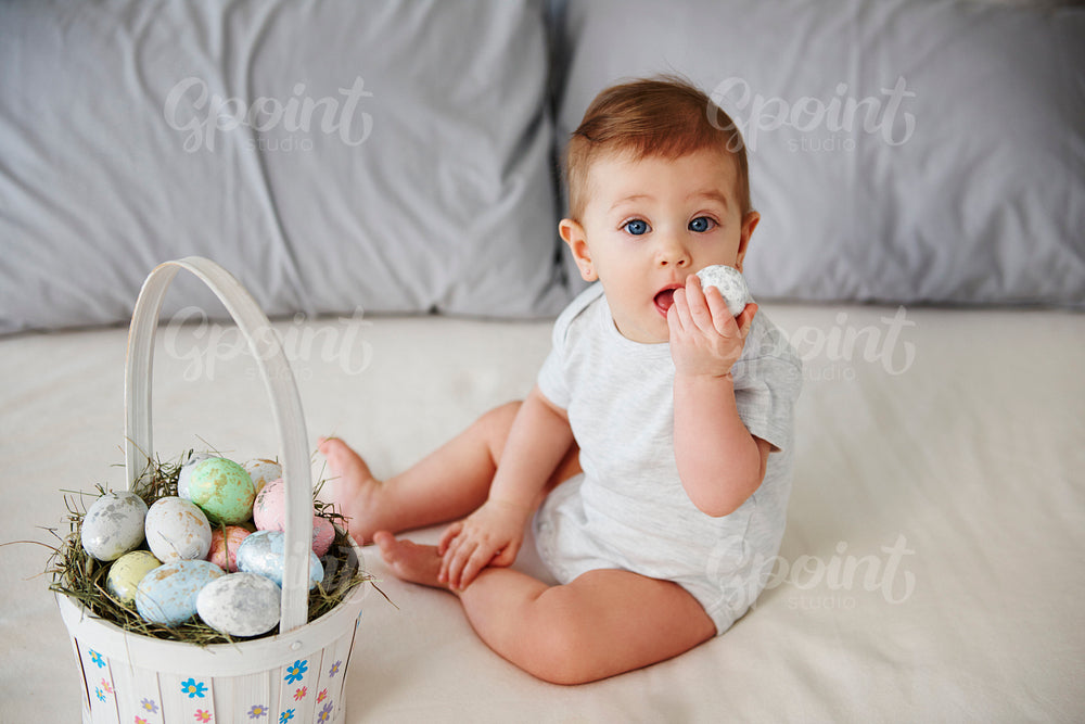 Playful baby eating easter egg on the bed