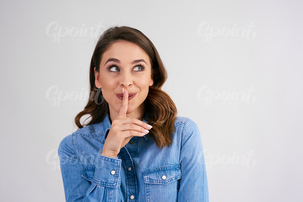 Woman with finger on lips looking up in studio shot