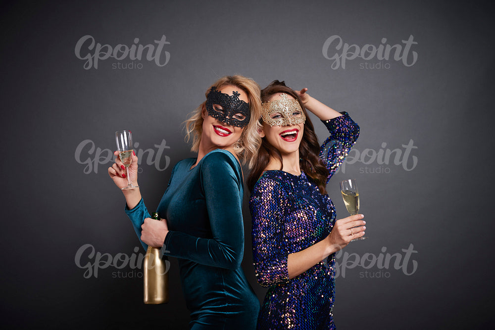 Women in masks drinking champagne in studio shot