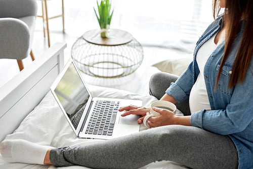 Pregnant woman using laptop while sitting on bed