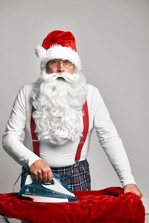 Shocked Santa Claus ironing trousers for Christmas