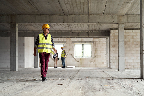 Wide image of caucasian senior engineer walking and holding plans on construction site