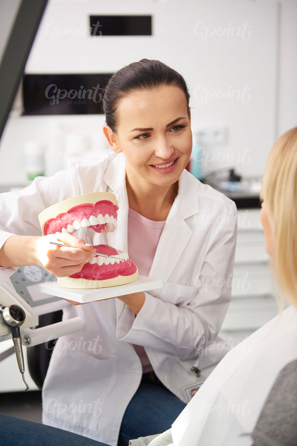 Smiling female dentist showing patient the artificial dentures