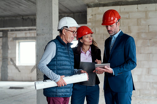 Group of three caucasian engineers and investors standing and discussing on construction site