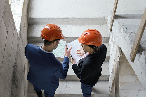 Female caucasian engineer and business woman holding document while walking stairs on construction site