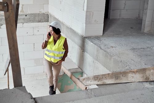 Waist up video of female caucasian engineer on the construction site talking on the phone and checking some documents